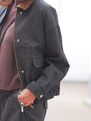 Nahaufnahme eines Outfits mit der OFF#DLY Jacke Denim Black: Eine dunkle, kastige Jeansjacke mit Cordkragen, kombiniert mit einem braunen Strickpullover, dunklen Utility-Hosen und mattschwarzen Perlen.