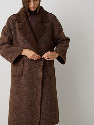 Person befestigt Knopf des BSB Mantel 215004 chocolate, langer, gerader Schnitt mit Bouclé-Futter, Reverskragen, zweireihiger Knopfleiste, großen Taschen und weiten Ärmeln.