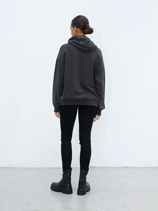 Person von hinten in minimalistischer, monochromer Kleidung, trägt das Outryght Sweater HAZ S. faded black, locker sitzend, kombiniert mit schwarzen Skinny-Jeans und klobigen Stiefeletten, Haare im tiefen Dutt.