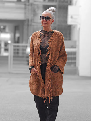 Frau trägt BSB Cardigan 215013 chocolate mit Fransen, lockerem Schnitt und Taschen. Kombiniert mit schwarzem Spitzenoberteil und Hosen, vermittelt sie einen stilvollen und selbstbewussten Look.