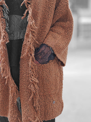 Eine Person trägt den BSB Cardigan 215013 chocolate: ein rustbrauner Teddy-Mantel mit Fransen, kombiniert mit einem schwarzen Spitzenoberteil und Spitzenhandschuhen, wobei eine Hand in der Tasche steckt.