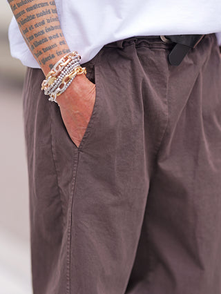 Nahaufnahme der OFF#DLY Hose Melania schoko, locker getragen mit schwarzem Gürtel. Einzigartige Details wie ein Text-Tattoo auf dem Unterarm und goldene Armbänder ergänzen den lässigen Look.