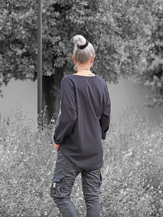 Person von hinten in einem lässigen OFF#DLY Sweat Solveig black mit funkelndem VOGUE-Schriftzug, lockerer Schnitt und überschnittene Schultern, stehend in einer natürlichen Umgebung.