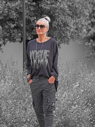Ältere Frau trägt modisches OFF#DLY Sweat Solveig black Sweatshirt mit glänzendem VOGUE Schriftzug, lockerer Passform und überschnittenen Schultern, kombiniert mit schwarzen Cargo-Hosen und auffälligem Schmuck.