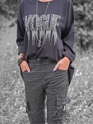 OFF#DLY Sweat Solveig black, locker geschnittenes schwarzes Sweatshirt mit glänzendem „VOGUF“-Schriftzug und funkelnden Applikationen. Getragen mit schwarzen Cargo-Hosen und Accessoires, vermittelt es lässigen Chic.