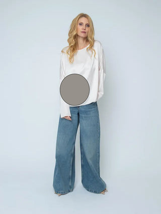 Frau trägt Emily Damenbluse taupe mit rundem Ausschnitt und überschnittenen Schultern. Kombiniert mit sehr weiten blauen Jeans und spitzen Absätzen. Grauer Patch über dem Mittelteil.