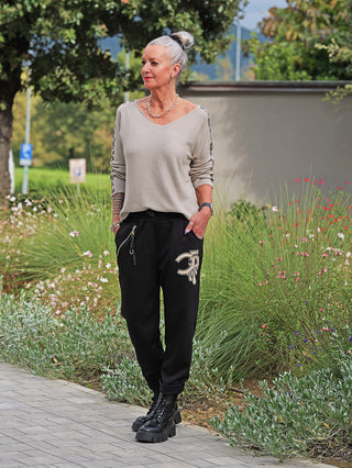 Ältere Frau trägt die OFF#DLY Joggpant Bonny black mit funkelnder Strassapplikation am Oberschenkel, kombiniert mit lässigen, schwarzen Chunky Boots auf einem gepflasterten Weg.