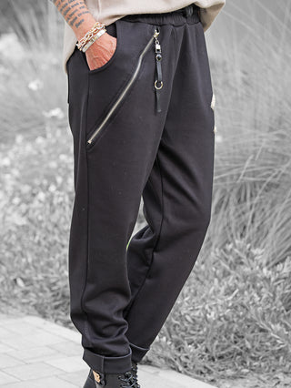 OFF#DLY Joggpant Bonny black mit diagonalem Reißverschluss, Lederriemen am Bund und Strass-Applikation am Oberschenkel. Gepaart mit schwarzen Schnürstiefeln und sichtbaren Armtattoos und Armbändern.