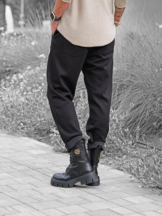 Person trägt OFF#DLY Joggpant Bonny black, relaxed-fit mit hochgerollten Bündchen, kombiniert mit klobigen Lederstiefeln. Sichtbare Strass-Applikation am Oberschenkel, ideal für lässigen Streetstyle.