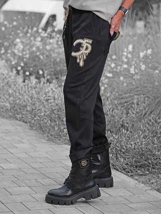 OFF#DLY Joggpant Bonny black in Nahaufnahme, zeigt schwarze Jogginghose mit Strass-Logo auf dem Oberschenkel, kombiniert mit klobigen schwarzen Stiefeln und einem grauen Oberteil, Hand in der Tasche.