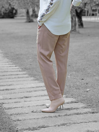 Person trägt OFF#DLY Joggpant Bonny beige, gerade geschnittene Hose mit Strass-Applikation, kombiniert mit spitzen Ankle-Boots. Perfekt für eleganten Casual-Look im Park auf Steinweg.