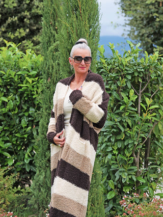 Ältere Frau trägt den OFF#DLY Cardigan Sandy brown Stripes mit breiten, horizontalen Streifen und offenem Schnitt, hält die Vorderkanten sanft, während sie zur Seite lächelt.