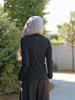 Person von hinten in einer stilvollen Haltung auf einem Weg, trägt OFF#DLY Rolli Agnes black, einen schmal geschnittenen schwarzen Langarm-Rolli mit feiner Ripp-Struktur und leichtem Stehkragen.