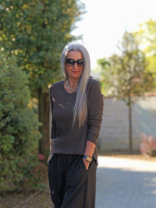 Ältere Frau trägt das OFF#DLY LS Alice schoko, ein schmal geschnittenes Longsleeve mit leichter Ripp-Struktur und offenen Kanten. Die entspannte, stilvolle Silhouette wird von Sonnenbrille und Accessoires betont.