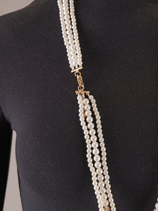 Die OFF#DLY Kunstperlenkette 3 Strang white/gold zeigt lange, mehrsträngige, weiße Perlen mit goldfarbenem Metall, drapiert über ein schwarzes Oberteil, ideal für elegante Anlässe.