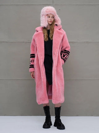 Junge Frau trägt #VDR Coat pink, einen übergroßen, rosa Fake-Fur-Mantel mit schwarzen Schriftzügen. Kombiniert mit einem passenden pinken Hut und schwarzen Stiefeln, perfekter Statement-Look für den Winter.