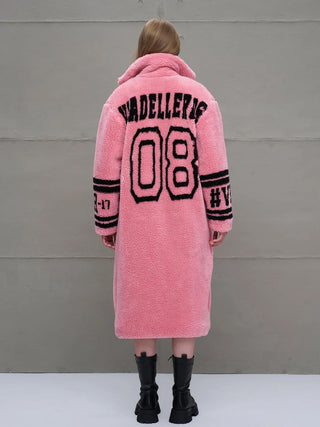 #VDR Coat pink: Rückansicht einer Person in einem langem, rosa Teddy-Fleece-Mantel mit schwarzen Streifen und Schriftzügen, darunter „VADELLERIS“ und „08“, kombiniert mit klobigen schwarzen Schnürstiefeln.