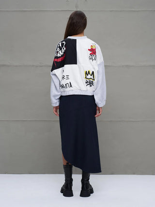 Person trägt #VDR Sweatjacke grey mel mit graffitiartigen Grafiken, kombiniert mit einem dunklen Rock und schwarzen Stiefeln. Die Jacke zeigt einen verspielten, urbanen Stil mit auffälligen Prints.