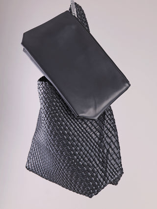Zwei schwarze Lederbeutel: Der glatte Clutch mit Reißverschluss liegt auf der größeren, geflochtenen OFF#DLY Flecht Tasche black, die eine geräumige Textur präsentiert.
