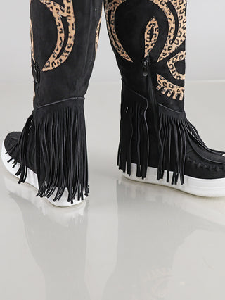 OFF#DLY Stiefel black aus schwarzem Kunstleder in Velour-Optik, mit Fransen, seitlichem Zipper und Leo-Applikationen, stehen auf reflektierendem Boden. Weiße, dicke Sohlen verleihen ihnen einen modernen Look.