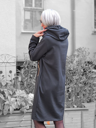 Person von hinten in langem, dunklem OFF#DLY Dress Belinda black mit Kapuze, silberweißem Haar, steht draußen, hält Kragen. Kombiniert mit dunklen Leggings für sportiv-femininen Streetstyle.