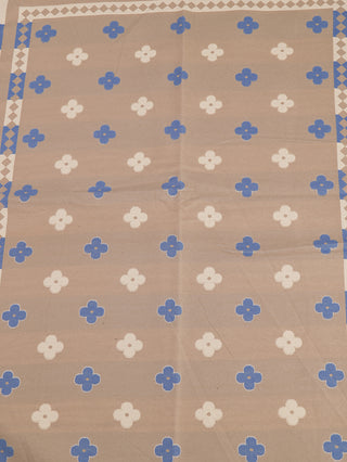 Der OFF#DLY Schal Britta blue/beige zeigt ein beiges Gewebe mit weißen und blauen vierblättrigen Motiven, einem geometrischen Rand in Blau-Weiß, und besteht aus 80% Viskose und 20% Wolle.