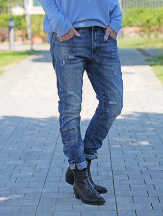 Person trägt OFF#DLY Denim Ines Midblue Destroy, eine moderne Jeans mit authentischen Destroy-Details, figurbetonter Passform und ohne Unterlegung, kombiniert mit schwarzen Lederstiefeletten für einen lässigen Look.