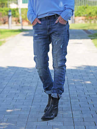 OFF#DLY Denim Ines Midblue Destroy Jeans mit authentischen Destroy-Details, schmalem Schnitt, umgeschlagenen Bündchen und sichtbaren Reparaturnähten, getragen mit schwarzen Lederstiefeln für einen lässigen, urbanen Look.