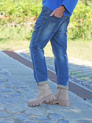 OFF#DLY Denim Dunja destroy Midblue Jeans, lässig mit umgeschlagenen Säumen und dezenten Destroyed-Details, getragen mit klobigen, tanfarbenen Boots auf einem gepflasterten Weg. Hände in den Taschen, silberne Ringe sichtbar.