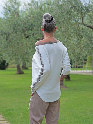 Person von hinten in OFF#DLY Pulli Brenda white mit schulterfreiem Design und glitzernden Strass auf Ärmeln. Kombiniert mit hellen, weiten Hosen, goldener Kette und Ohrringen.