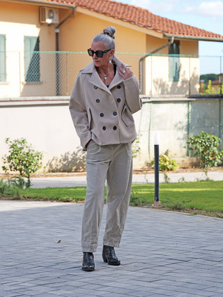 Eine Frau trägt die OFF#DLY Jacke Valeska creme, ein doppelt geknöpftes, elegantes Kleidungsstück mit Reverskragen und modischen Schulterdetails, kombiniert mit passenden Hosen und schwarzen Stiefeletten.
