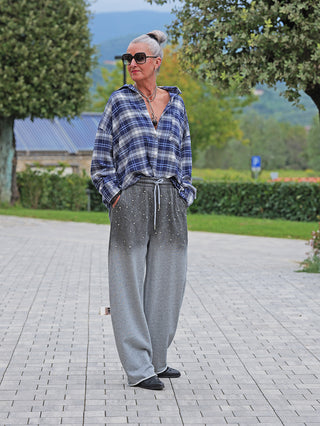 Ältere Frau in OFF#DLY Bluse Greta blau kariert, weit offen getragen, kombiniert mit grauen, weit geschnittenen Sweatpants.