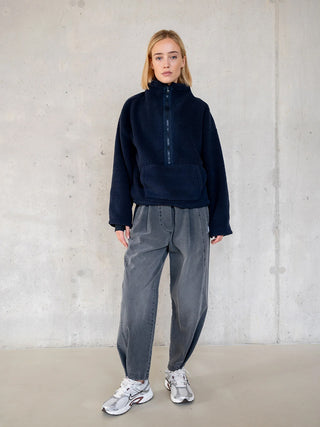 Junge Frau trägt Penn&Ink Denim WZ25811 grau, eine Barrel-Jeans mit elastischem Bund und Seitentaschen, präsentiert vor einer glatten Betonwand.