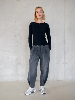 Junge Frau trägt Penn&Ink Denim WZ25811 grau: hochgeschnittene, locker sitzende Hose mit Falten vorne und Seitentaschen, kombiniert mit schwarzem Henley-Top und weißen Sneakers.