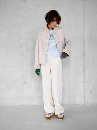 Person trägt die Penn&Ink Jacket W25c321 ecru, eine kurz geschnittene Shearling-Jacke mit Knebelverschlüssen, über einem grauen T-Shirt und weiten, weißen Hosen.