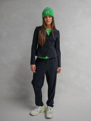 Penn&Ink Trousers antra: Die junge Frau trägt schwarze, locker geschnittene Penn&Ink Trousers antra, kombiniert mit einem eleganten schwarzen Blazer und auffälligen weißen Sneakers, ideal für vielseitige Looks.