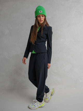 Penn&Ink Trousers antra: Locker geschnittene, schwarze Hose mit tiefem Schritt und elastischem Bund, kombiniert mit einem schwarzen Blazer und auffälligen Sneakers, verkörpert moderne Eleganz und Komfort.