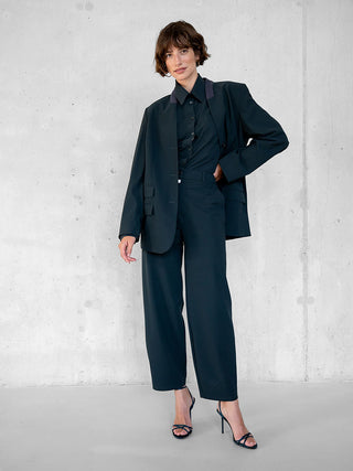 Frau trägt den Penn&Ink Blazer antra mit kastigem Schnitt, markanten Schultern, kontrastierendem Kragen und Vier-Knopf-Verschluss, kombiniert mit schwarzem Hemd und Hose für einen minimalistischen Business-Look.