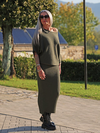 Ältere Frau trägt den OFF#DLY Pulli Ellen khaki mit lockerer Passform und Fledermausärmeln, kombiniert mit passendem Rock, silbernen Accessoires und schwarzen Stiefeln, präsentiert stilvollen, femininen Chic.