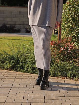 Person trägt den OFF#DLY Rock Linda grey, einen grauen, gerippten Midi-Rock mit elastischem Bund. Kombiniert mit klobigen schwarzen Stiefeln, bietet er eine lässige und elegante Silhouette.