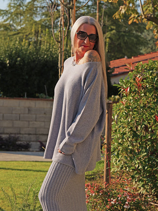 Die Person trägt den OFF#DLY Longpulli Rosi grey, ein lockeres, off-shoulder Feinstrick-Kleidungsstück, das einen gemütlichen und stilvollen Look verkörpert, perfekt für entspannte, elegante Casual-Outfits.