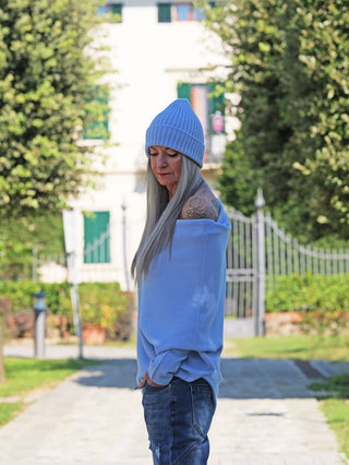 Älterer Erwachsener trägt den OFF#DLY Pulli Irene asymetric lightblue mit freiliegender Schulter und Tattoo, kombiniert mit Jeans und Beanie, auf einem Gartenweg stehend, zeigt einen ruhigen, nachdenklichen Ausdruck.