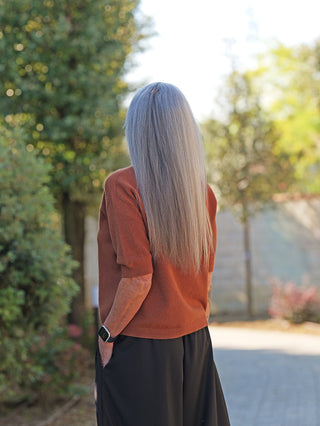 Person mit langen grauen Haaren trägt den OFF#DLY Pulli Tina camel, ein kurzärmeliges, schmal geschnittenes Strick-Oberteil, kombiniert mit einer Smartwatch und weiten schwarzen Hosen.