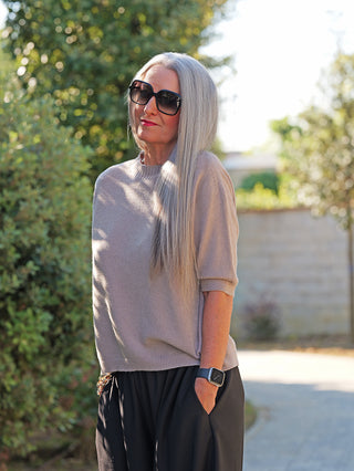 Frau trägt den OFF#DLY Pulli Tina beige, ein schmal geschnittenes Kurzarm-Basic, kombiniert mit schwarzen Hosen. Perfekt für einen modernen, vielseitigen Look in der Natur.