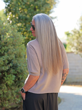 Eine Person trägt den OFF#DLY Pulli Tina beige, ein kurzärmliges, fein geschnittenes Oberteil, kombiniert mit einer schwarzen Hose. Der Pulli verleiht eine feminine Silhouette und einen modernen Look.