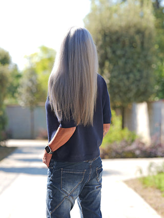 Person von hinten in OFF#DLY Pulli Tina darkblue, kurzärmelig, schmal geschnitten. Die Hände in den Taschen, auf sonnigem Weg stehend. Ideal für einen modernen, vielseitigen Look.