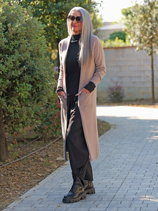 Person trägt den OFF#DLY Strickmantel Laura beige, offenen Schnitt, mit Taschen, über schwarzem Outfit und Stiefeln, stehend auf Gehweg, umgeben von Bäumen.