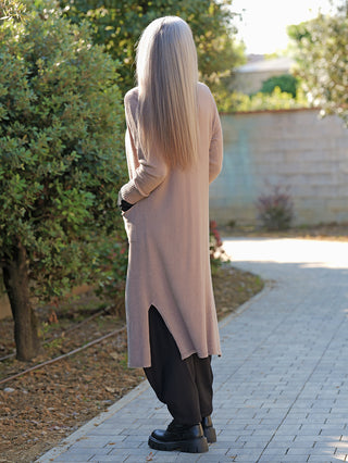 Person von hinten auf einem Weg, trägt den OFF#DLY Strickmantel Laura beige, einen langen, offenen Cardigan über schwarzen Hosen, kombiniert mit klobigen schwarzen Stiefeln.