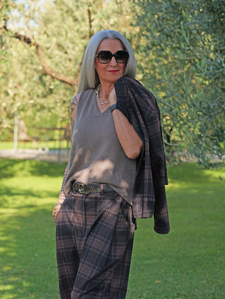Die stilvolle Frau trägt das OFF#DLY Stricktop Susi taupe, ein ärmelloses, graues Strickoberteil mit V-Ausschnitt, kombiniert mit einer lockeren, karierten Hose und einem passenden Blazer.