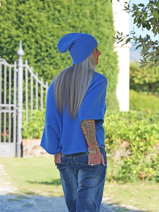 Person von hinten mit seitlichem Profil trägt den OFF#DLY Pulli Ellen denimblue, kombiniert mit einer passenden Mütze. Lang graues Haar, Tattoo am rechten Unterarm und silberne Accessoires ergänzen den Look.